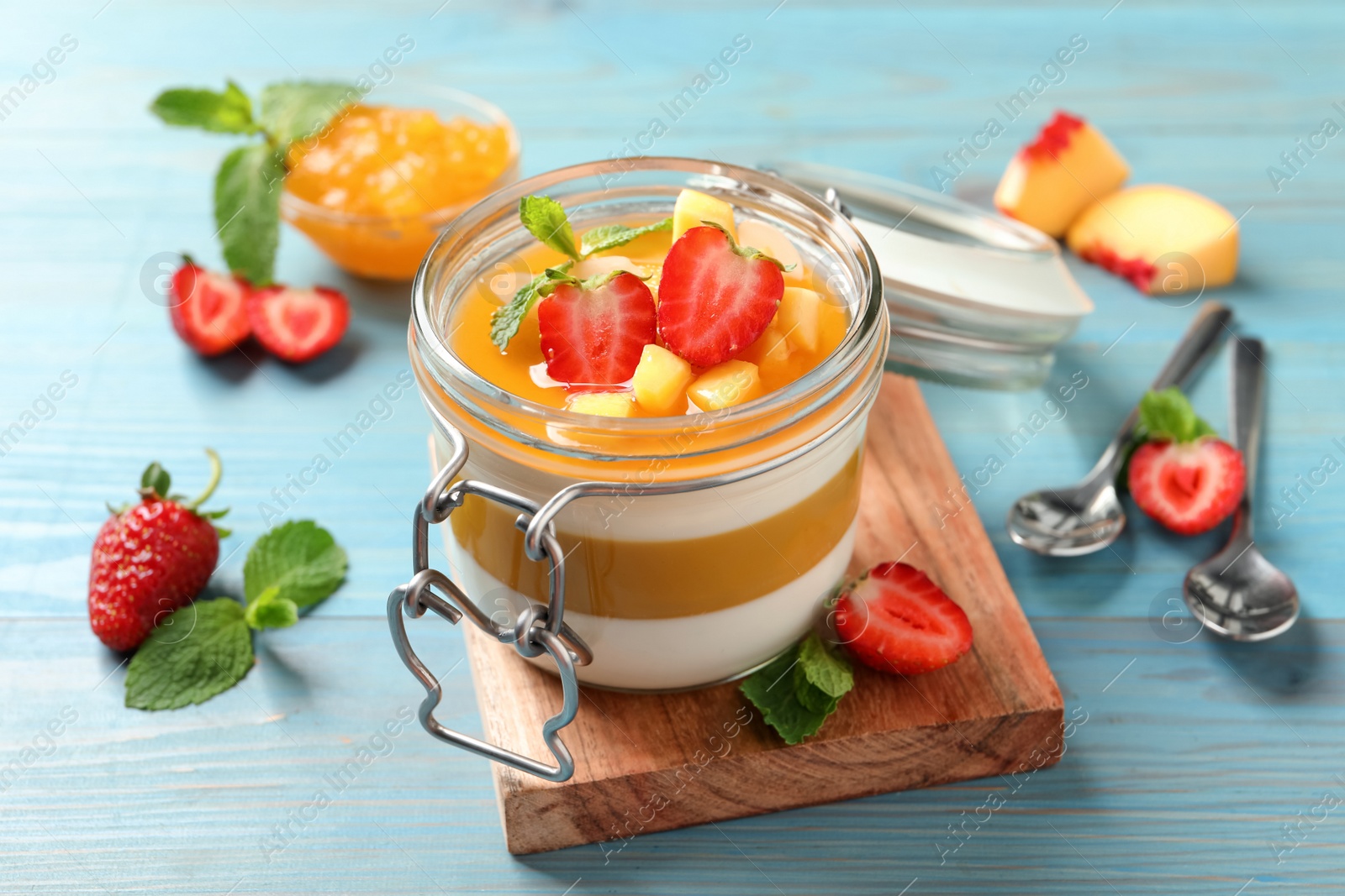 Delicious panna cotta with mango coulis and fresh fruit pieces on light blue wooden table Photo of Delicious panna cotta with mango coulis and fresh fruit pieces on light blue wooden table