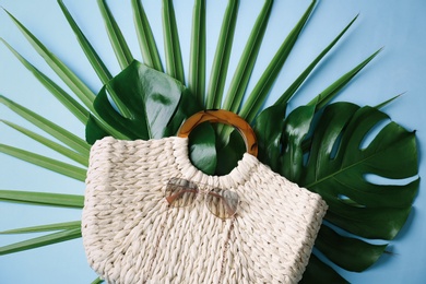 Elegant woman's straw bag with tropical leaves and sunglasses on light blue background, top view Photo of Elegant woman's straw bag with tropical leaves and sunglasses on light blue background, top view