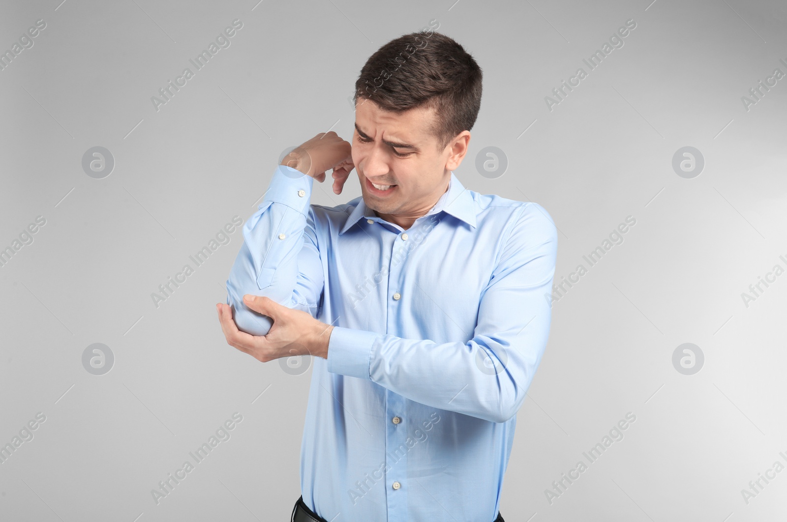 Young man suffering from pain in elbow on light background Photo of Young man suffering from pain in elbow on light background