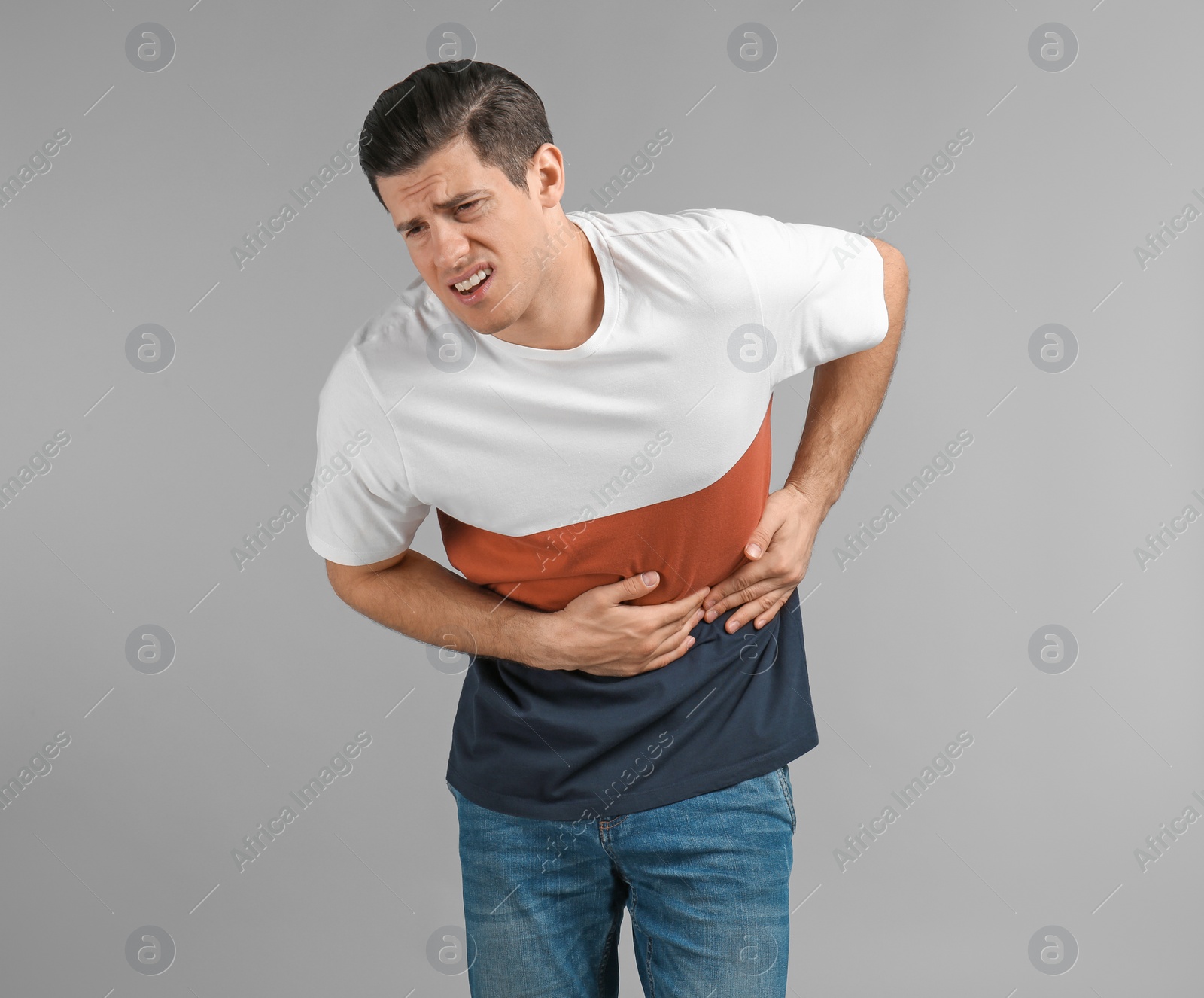 Young man suffering from abdominal pain on grey background Photo of Young man suffering from abdominal pain on grey background
