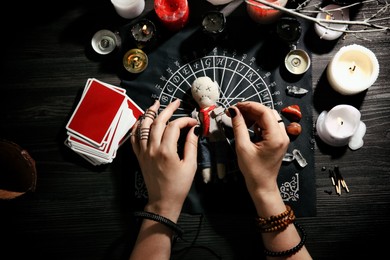 Woman stabbing voodoo doll with needle at table, closeup. Curse ceremony Photo of Woman stabbing voodoo doll with needle at table, closeup. Curse ceremony