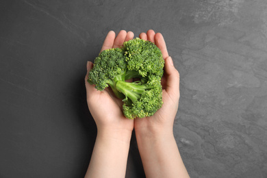 Woman holding fresh green broccoli over black table, top view Photo of Woman holding fresh green broccoli over black table, top view