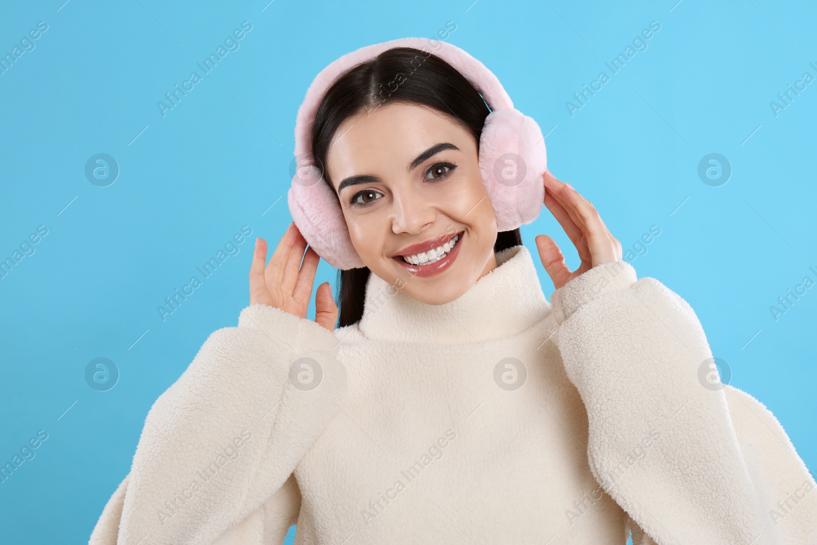 Beautiful young woman wearing earmuffs on light blue background Photo of Beautiful young woman wearing earmuffs on light blue background