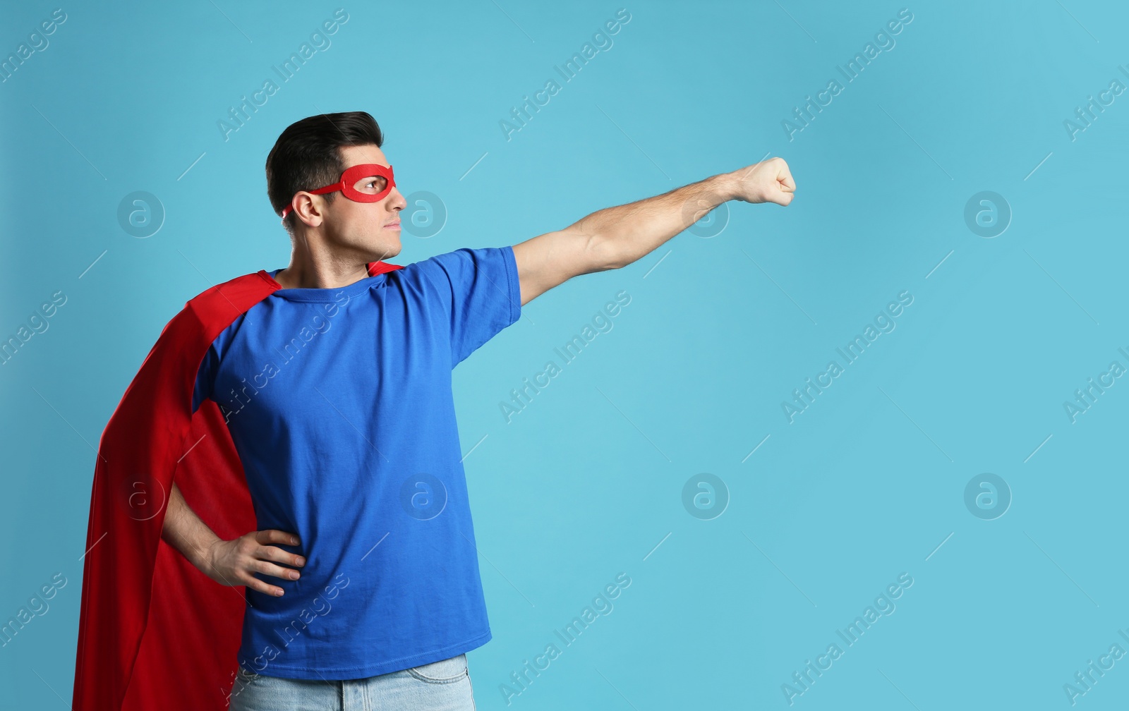 Man wearing superhero cape and mask on light blue background Photo of Man wearing superhero cape and mask on light blue background