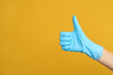 Doctor in medical gloves showing thumb up on yellow background, closeup. Space for text Photo of Doctor in medical gloves showing thumb up on yellow background, closeup. Space for text