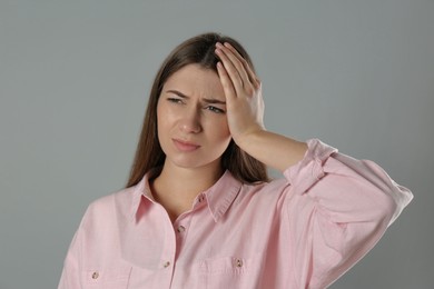 Young woman suffering from migraine on grey background Photo of Young woman suffering from migraine on grey background