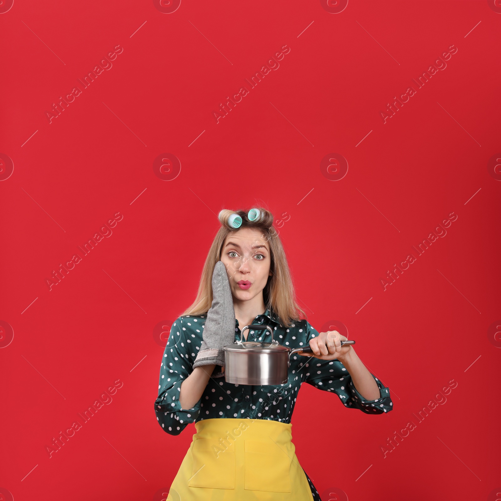 Young housewife with saucepan on red background Photo of Young housewife with saucepan on red background