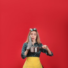 Young housewife with saucepan on red background Photo of Young housewife with saucepan on red background