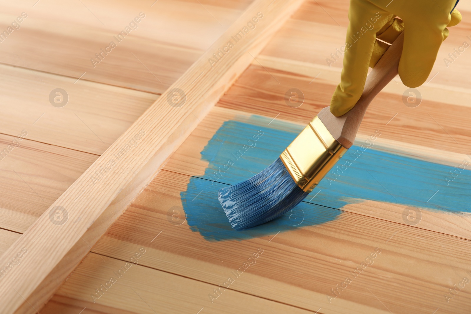 Worker applying blue paint onto wooden surface, closeup Photo of Worker applying blue paint onto wooden surface, closeup
