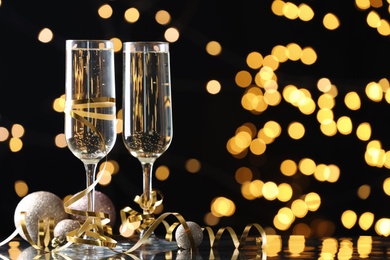 Glasses of champagne, Christmas decor and serpentine streamers against black background with blurred lights. Space for text Photo of Glasses of champagne, Christmas decor and serpentine streamers against black background with blurred lights. Space for text