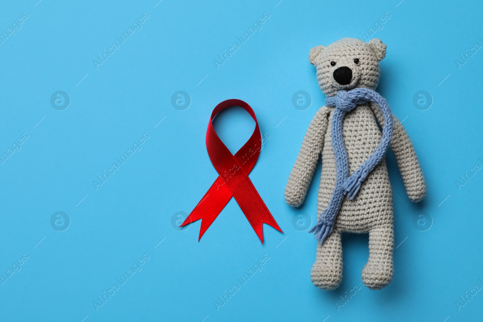 Cute knitted toy bear and red ribbon on blue background, flat lay with space for text. AIDS disease awareness Photo of Cute knitted toy bear and red ribbon on blue background, flat lay with space for text. AIDS disease awareness
