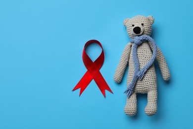 Cute knitted toy bear and red ribbon on blue background, flat lay with space for text. AIDS disease awareness Photo of Cute knitted toy bear and red ribbon on blue background, flat lay with space for text. AIDS disease awareness