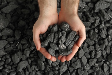 Man holding coal in hands over pile, top view Photo of Man holding coal in hands over pile, top view