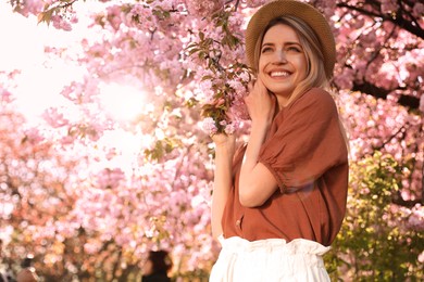 Young woman wearing stylish outfit near blossoming sakura in park. Fashionable spring look Photo of Young woman wearing stylish outfit near blossoming sakura in park. Fashionable spring look