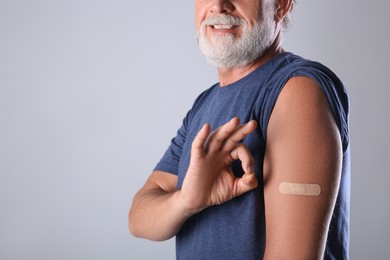 Senior man showing arm with bandage after vaccination on grey background, closeup Photo of Senior man showing arm with bandage after vaccination on grey background, closeup