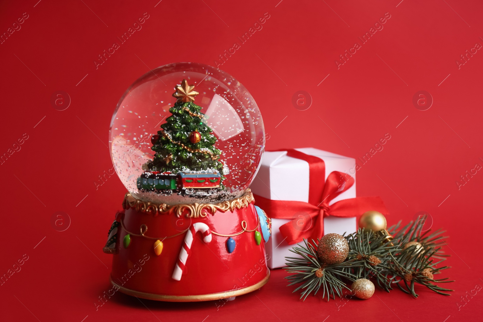 Beautiful snow globe and Christmas decor on red background Photo of Beautiful snow globe and Christmas decor on red background