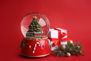 Beautiful snow globe and Christmas decor on red background Photo of Beautiful snow globe and Christmas decor on red background