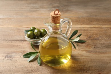 Glass jug of oil, ripe olives and green leaves on wooden table, closeup Photo of Glass jug of oil, ripe olives and green leaves on wooden table, closeup