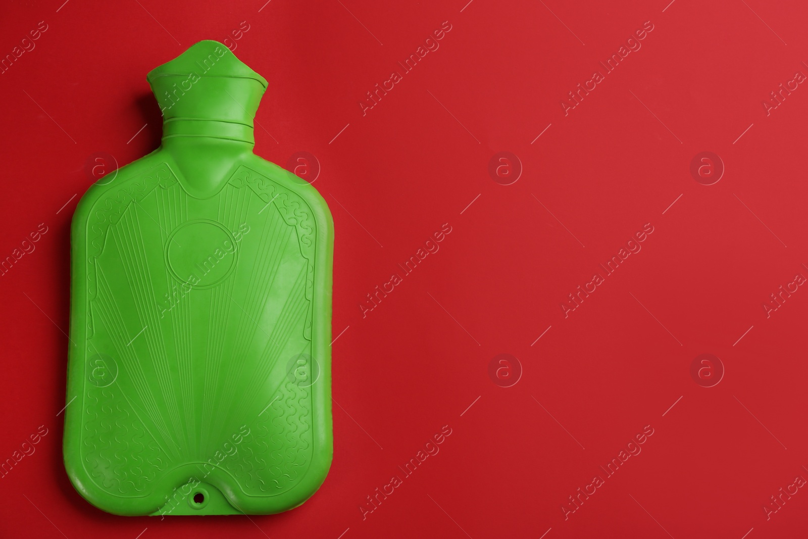 Photo of Green rubber hot water bottle on red background, top view. Space for text