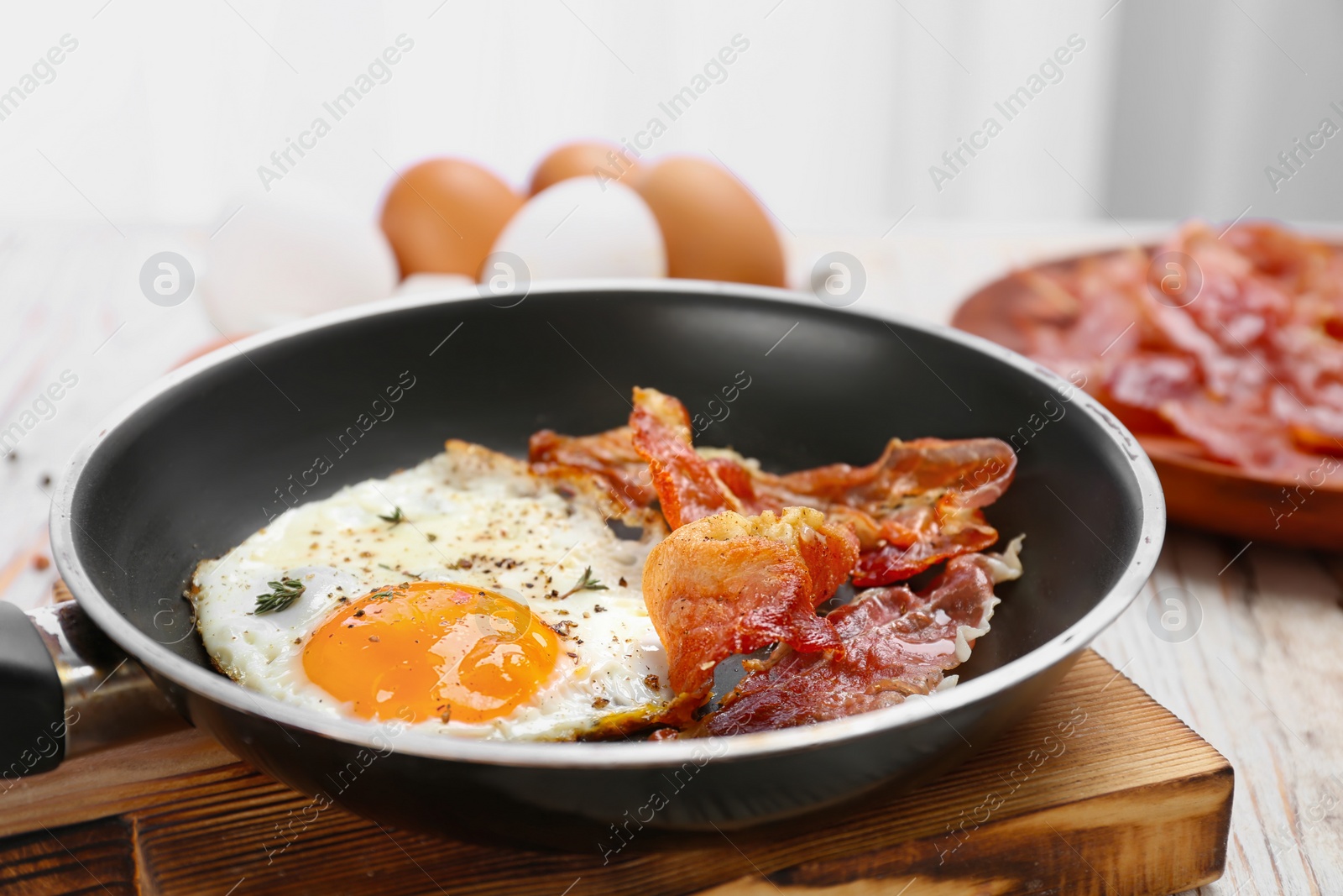 Frying pan with fried egg and bacon on wooden board, closeup Photo of Frying pan with fried egg and bacon on wooden board, closeup