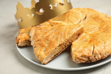 Traditional galette des Rois with paper crown on light grey marble table Photo of Traditional galette des Rois with paper crown on light grey marble table