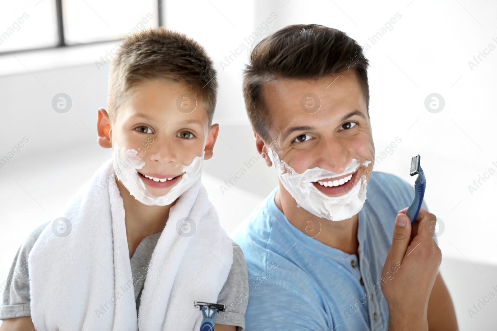 Happy father and son with shaving foam on their faces in bathroom Photo of Happy father and son with shaving foam on their faces in bathroom
