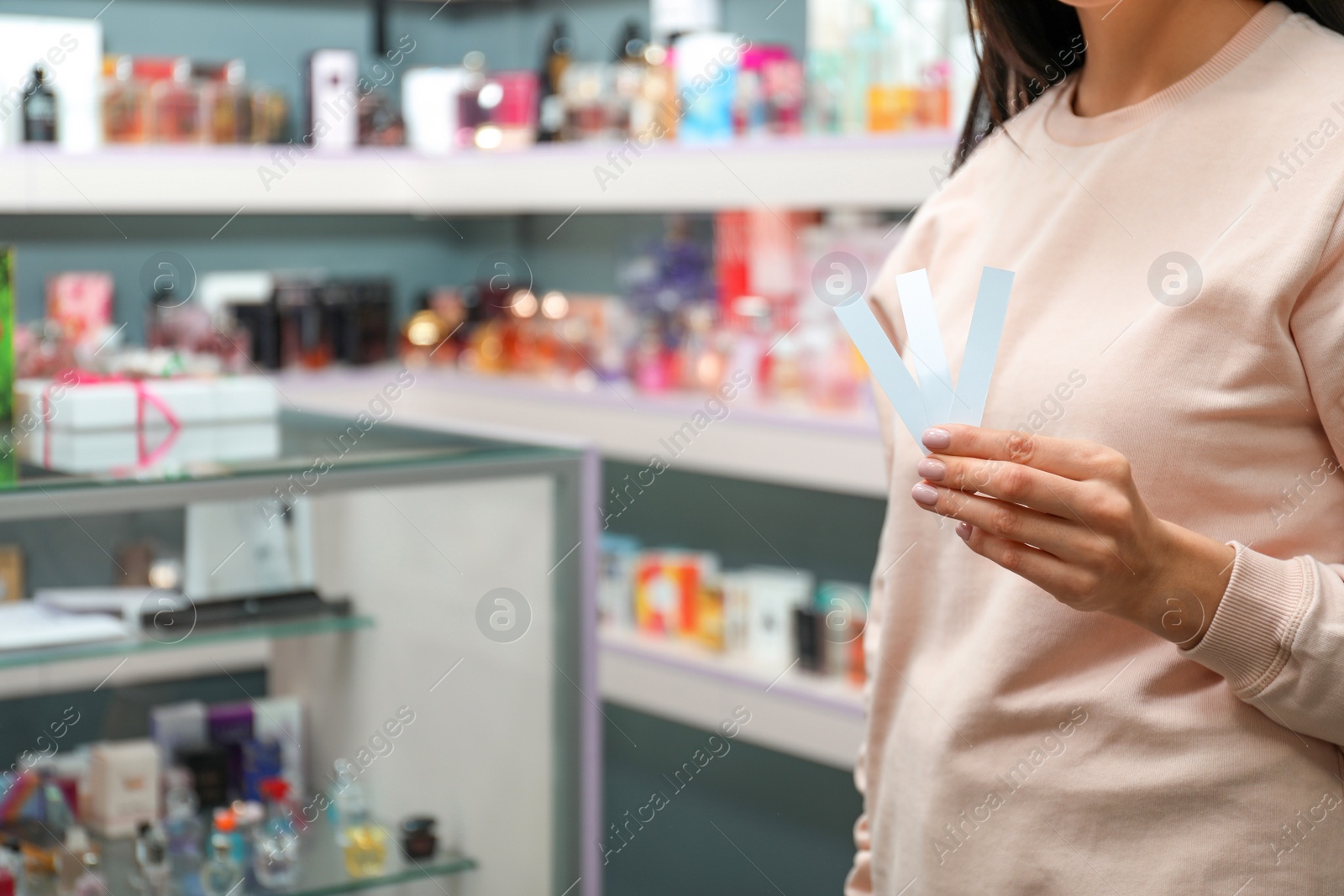 Young woman holding perfume testing stripes in shop, closeup. Space for text Photo of Young woman holding perfume testing stripes in shop, closeup. Space for text