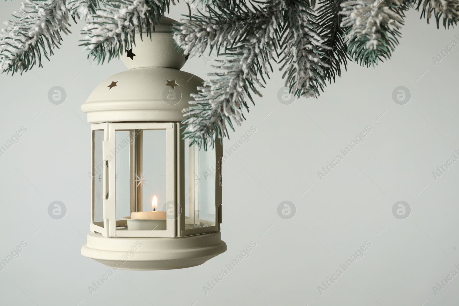 Christmas lantern with candle hanging on snowy fir tree branch against light background. Space for text Photo of Christmas lantern with candle hanging on snowy fir tree branch against light background. Space for text