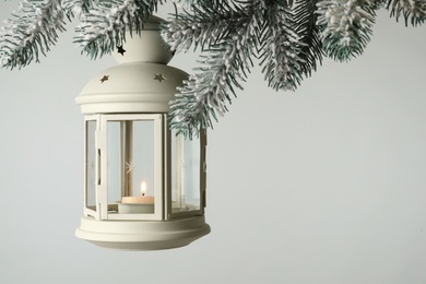 Christmas lantern with candle hanging on snowy fir tree branch against light background. Space for text Photo of Christmas lantern with candle hanging on snowy fir tree branch against light background. Space for text