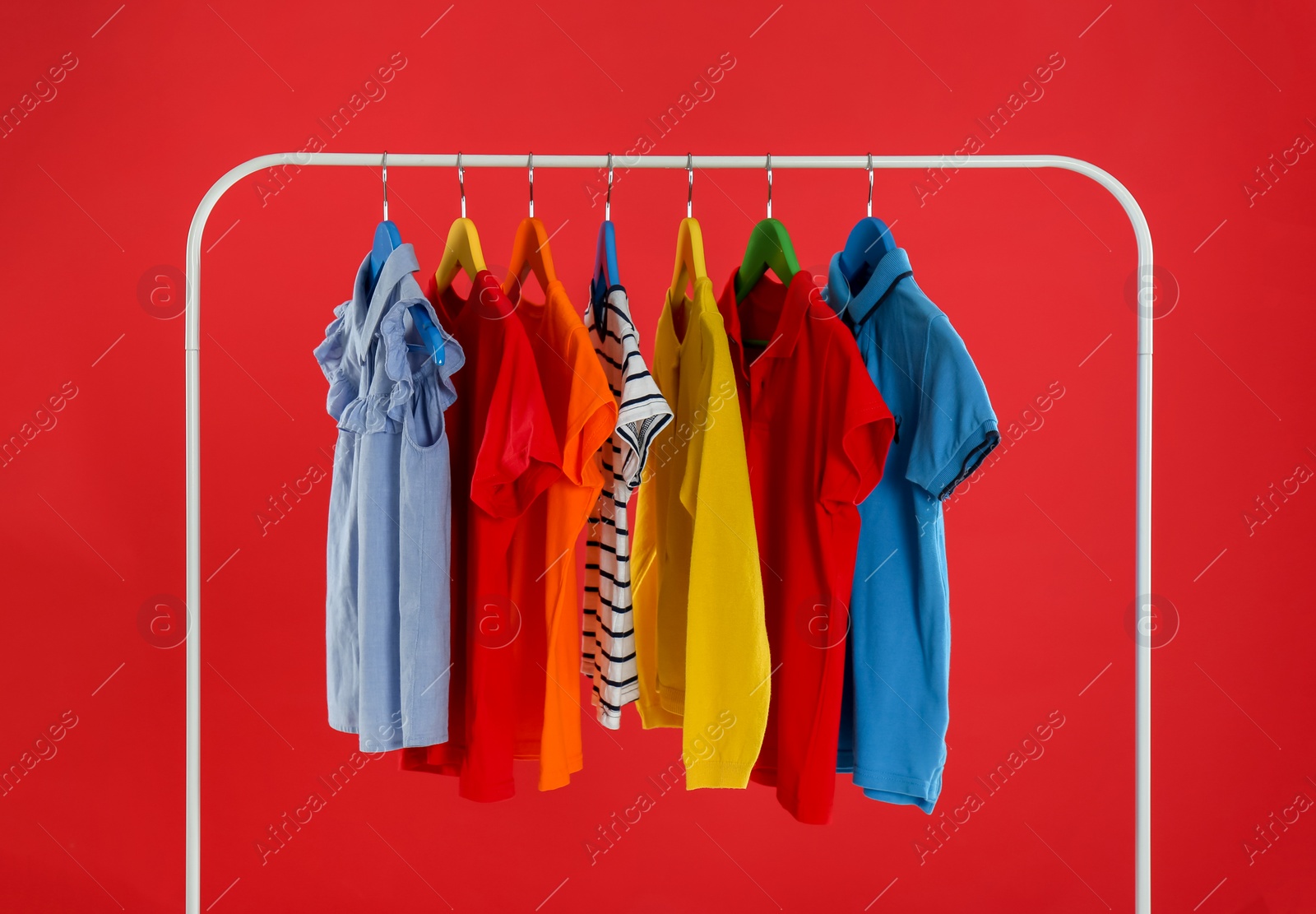 Rack with stylish children clothes on red background Photo of Rack with stylish children clothes on red background