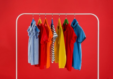 Rack with stylish children clothes on red background Photo of Rack with stylish children clothes on red background