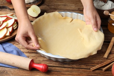 Woman putting dough for apple pie into baking dish at wooden table, closeup Photo of Woman putting dough for apple pie into baking dish at wooden table, closeup