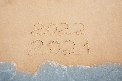 Dates written on sandy beach. 2021 washed by sea wave as New 2022 Year coming, above view Photo of Dates written on sandy beach. 2021 washed by sea wave as New 2022 Year coming, above view
