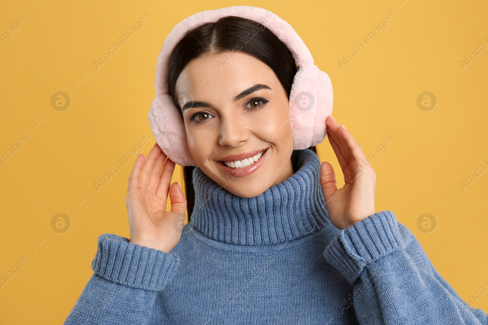 Beautiful young woman wearing earmuffs on yellow background Photo of Beautiful young woman wearing earmuffs on yellow background