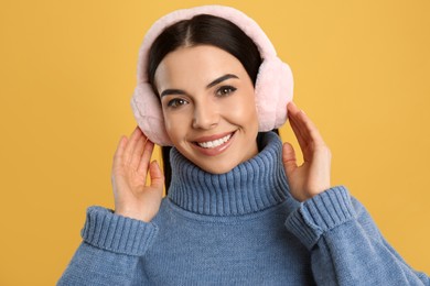 Beautiful young woman wearing earmuffs on yellow background Photo of Beautiful young woman wearing earmuffs on yellow background