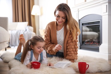 Happy woman and her daughter reading book near fireplace at home Photo of Happy woman and her daughter reading book near fireplace at home
