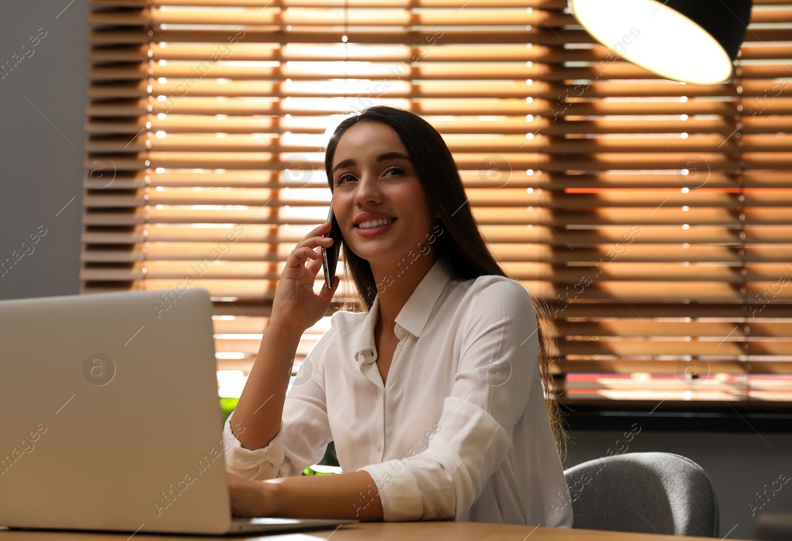 Woman with modern smartphone and laptop at wooden table in office. Searching information Photo of Woman with modern smartphone and laptop at wooden table in office. Searching information
