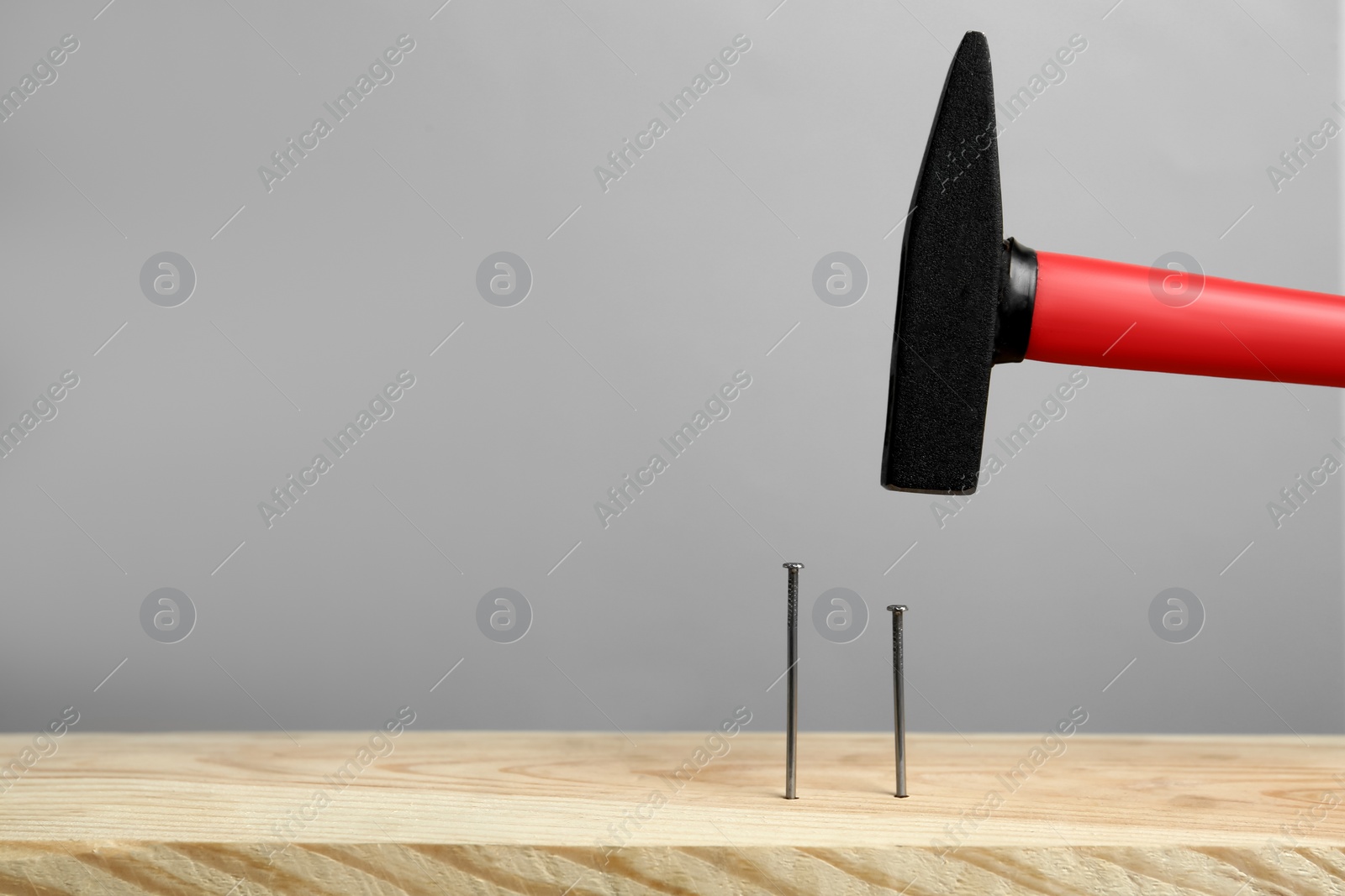 Hammering nail into wooden surface against grey background, space for text Photo of Hammering nail into wooden surface against grey background, space for text