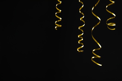 Shiny golden serpentine streamers on black background. Space for text Photo of Shiny golden serpentine streamers on black background. Space for text