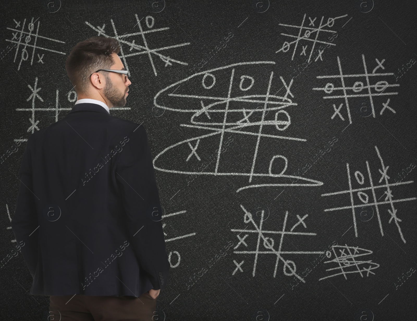 Young businessman in elegant suit near blackboard with drawn tic tac toe game Image of Young businessman in elegant suit near blackboard with drawn tic tac toe game