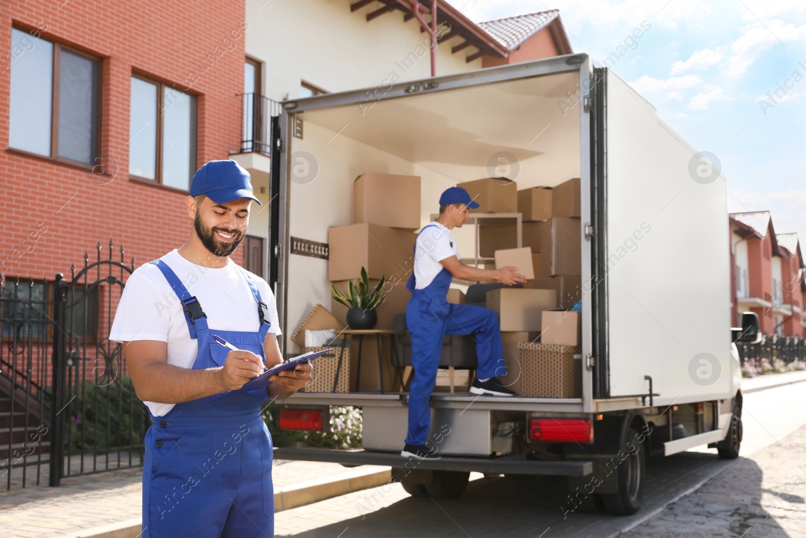 Moving service workers outdoors, unloading boxes and checking list Photo of Moving service workers outdoors, unloading boxes and checking list