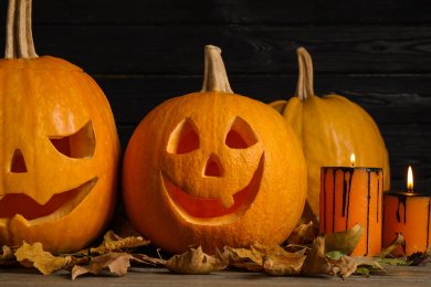 Pumpkins with scary faces and burning candles on black wooden background. Halloween traditional decor Photo of Pumpkins with scary faces and burning candles on black wooden background. Halloween traditional decor