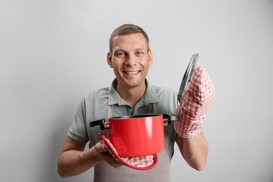 Happy man with cooking pot on light grey background Photo of Happy man with cooking pot on light grey background