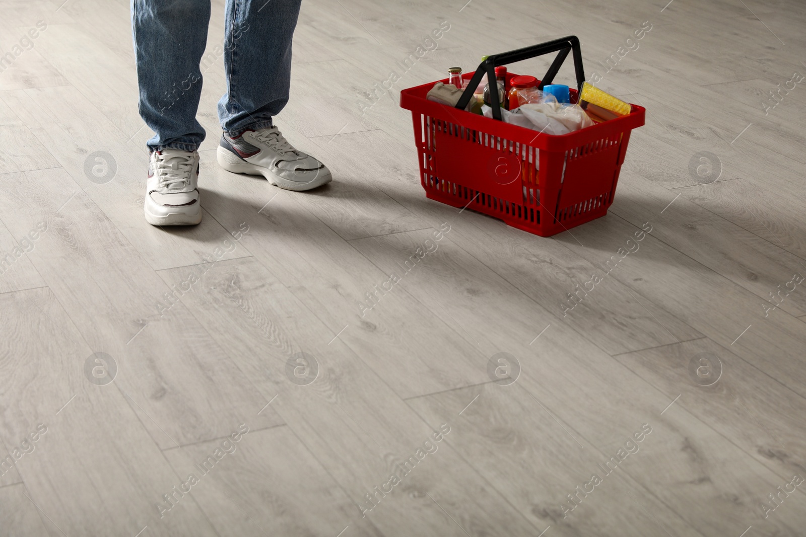 Woman and shopping basket with groceries on wooden floor, closeup. Space for text Photo of Woman and shopping basket with groceries on wooden floor, closeup. Space for text