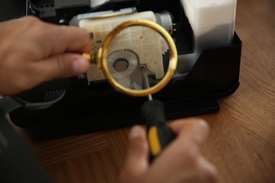 Repairman with magnifying glass and screwdriver fixing modern printer, closeup Photo of Repairman with magnifying glass and screwdriver fixing modern printer, closeup
