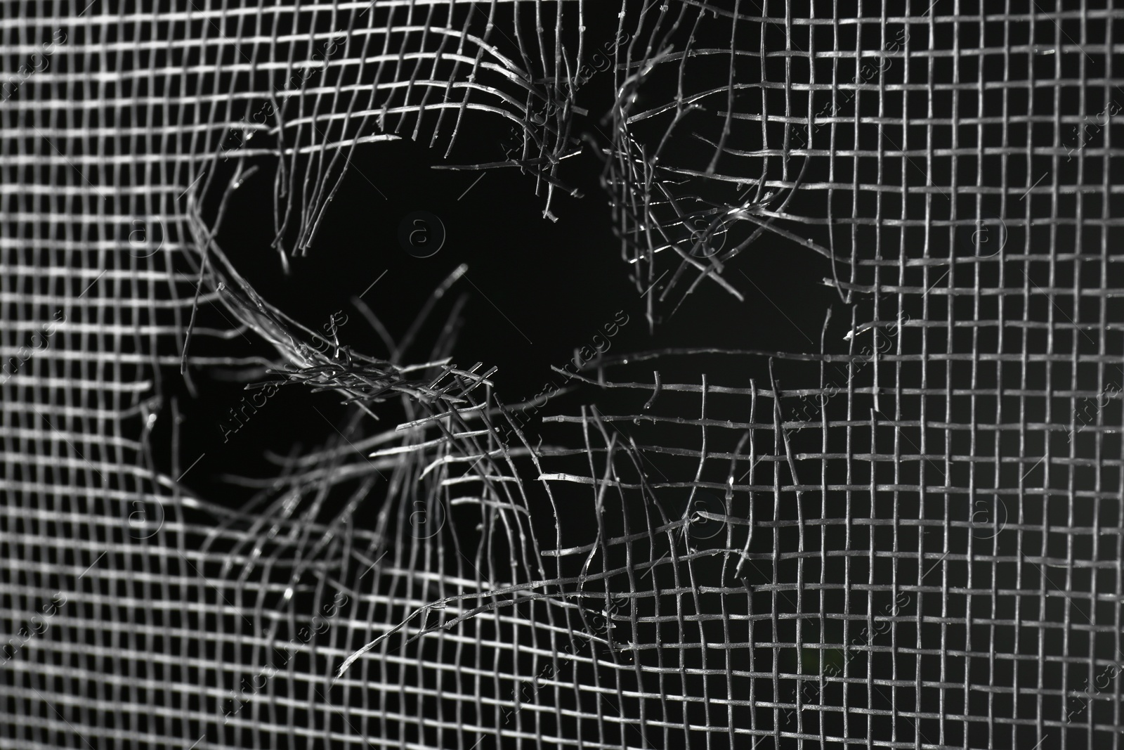 Photo of Torn window screen against black background, closeup