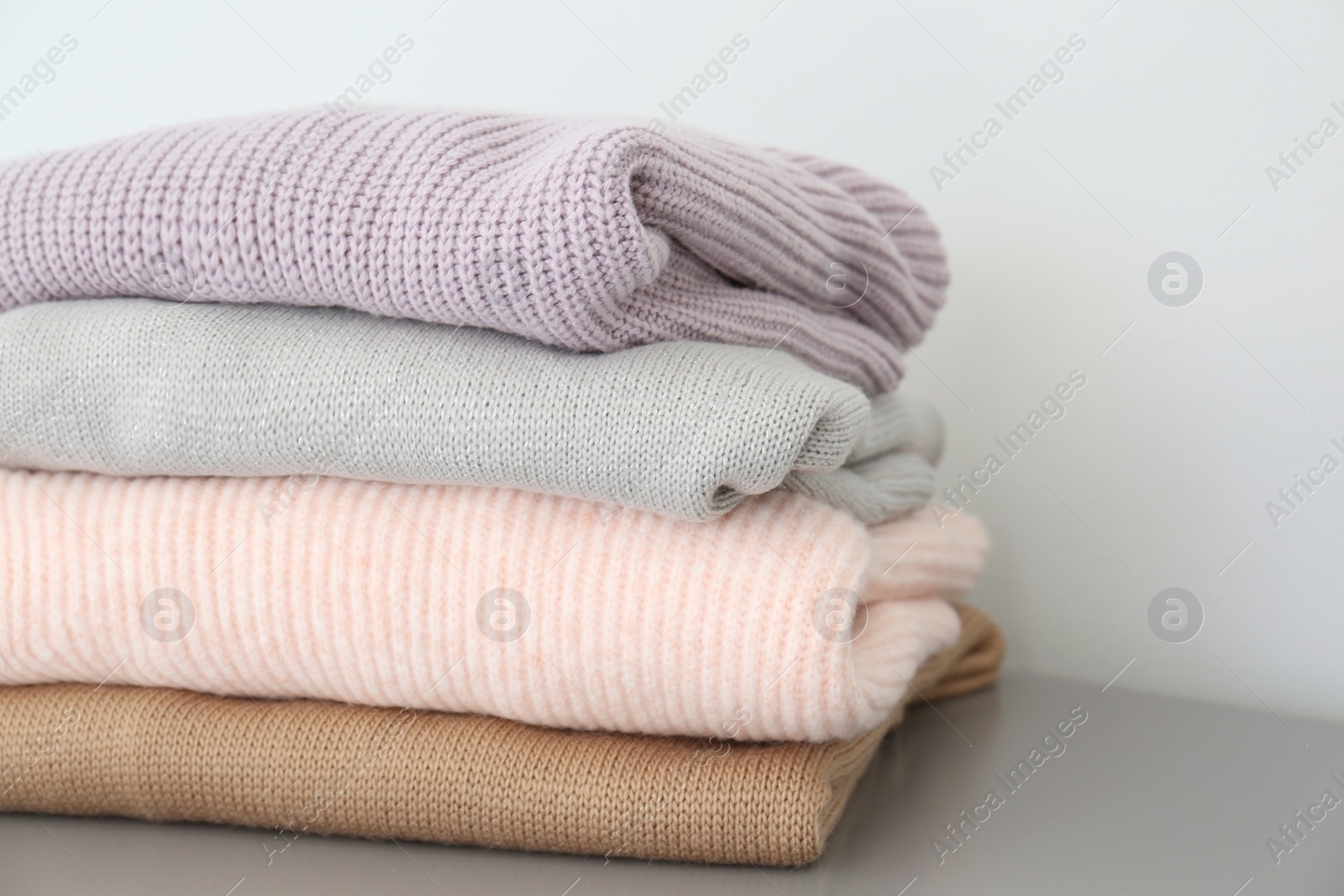 Stack of folded warm knitted sweaters on grey table, closeup Photo of Stack of folded warm knitted sweaters on grey table, closeup