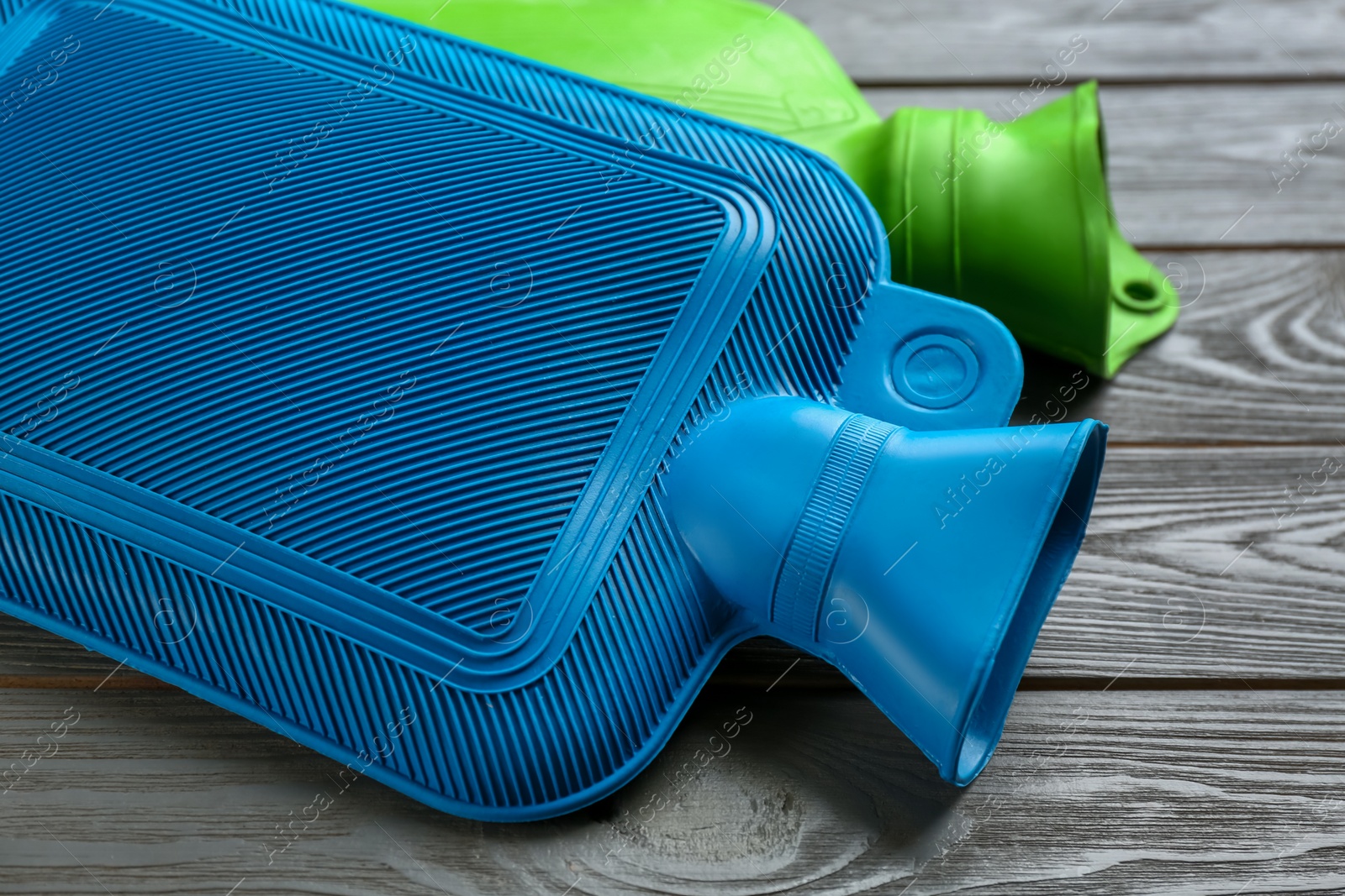 Photo of Rubber hot water bottles on grey wooden background, closeup