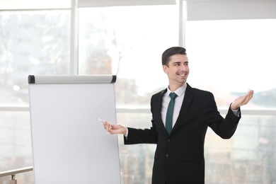 Business trainer giving presentation on flip chart board indoors Photo of Business trainer giving presentation on flip chart board indoors