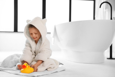 Photo of Cute little girl near tub in bathroom. Space for text